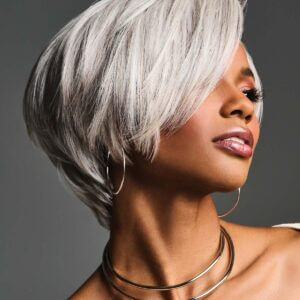 A woman with a chic platinum blonde bob hairstyle and silver hoop earrings, wearing a choker necklace, poses against a gray background.